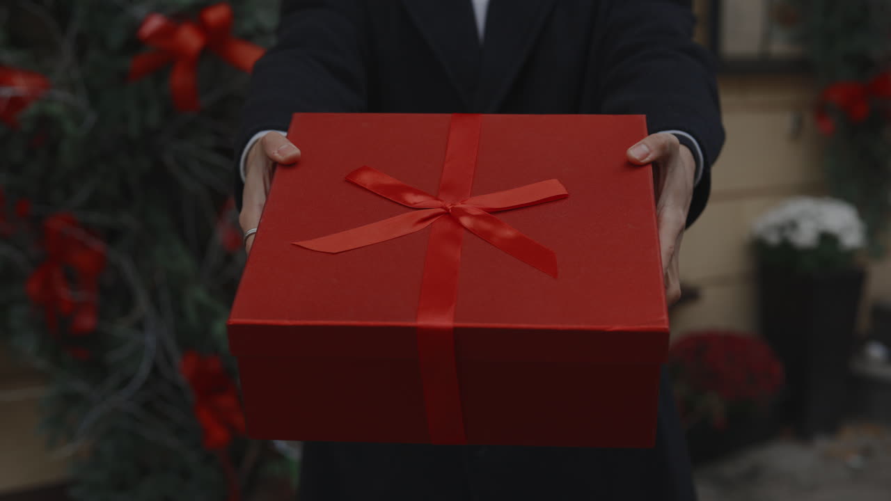 Person holding out a red gift box with a red ribbon