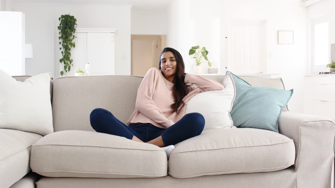 Smiling woman relaxing on cozy sofa at home, enjoying peaceful moment