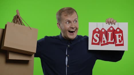 surprised guy showing shopping bags and sale word, looking astonished by low cost purchase, discount