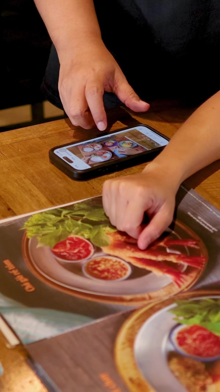 To personer bruger en smartphone til at vælge retter fra en digital menu i hyggelige omgivelser på en café i Bangkok.