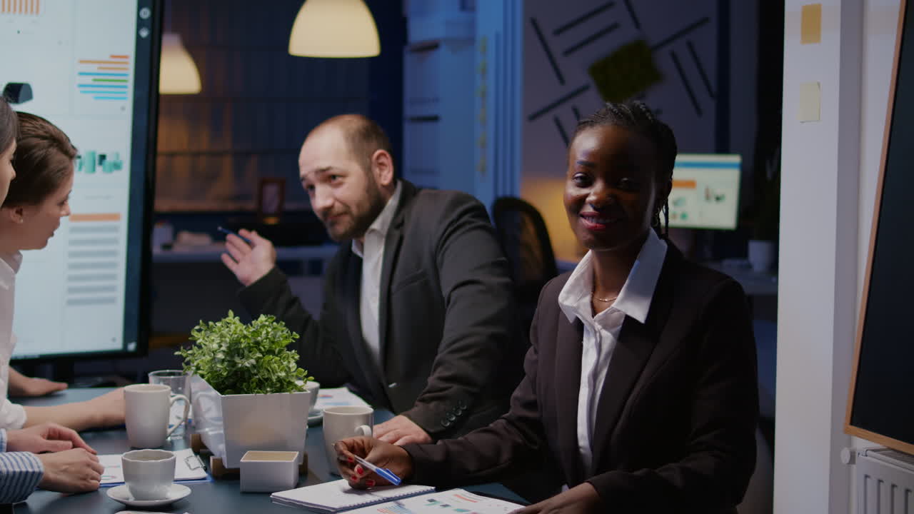 Portrait of focused smiling african woman sitting at desk in company office meeting room