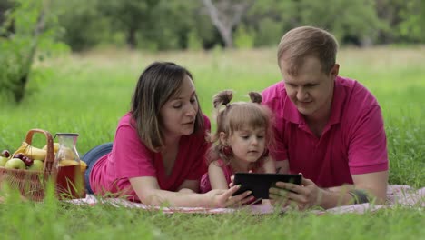 Family-weekend-picnic.-Daughter-child-girl-with-mother-and-father-watching-online-movies-on-tablet