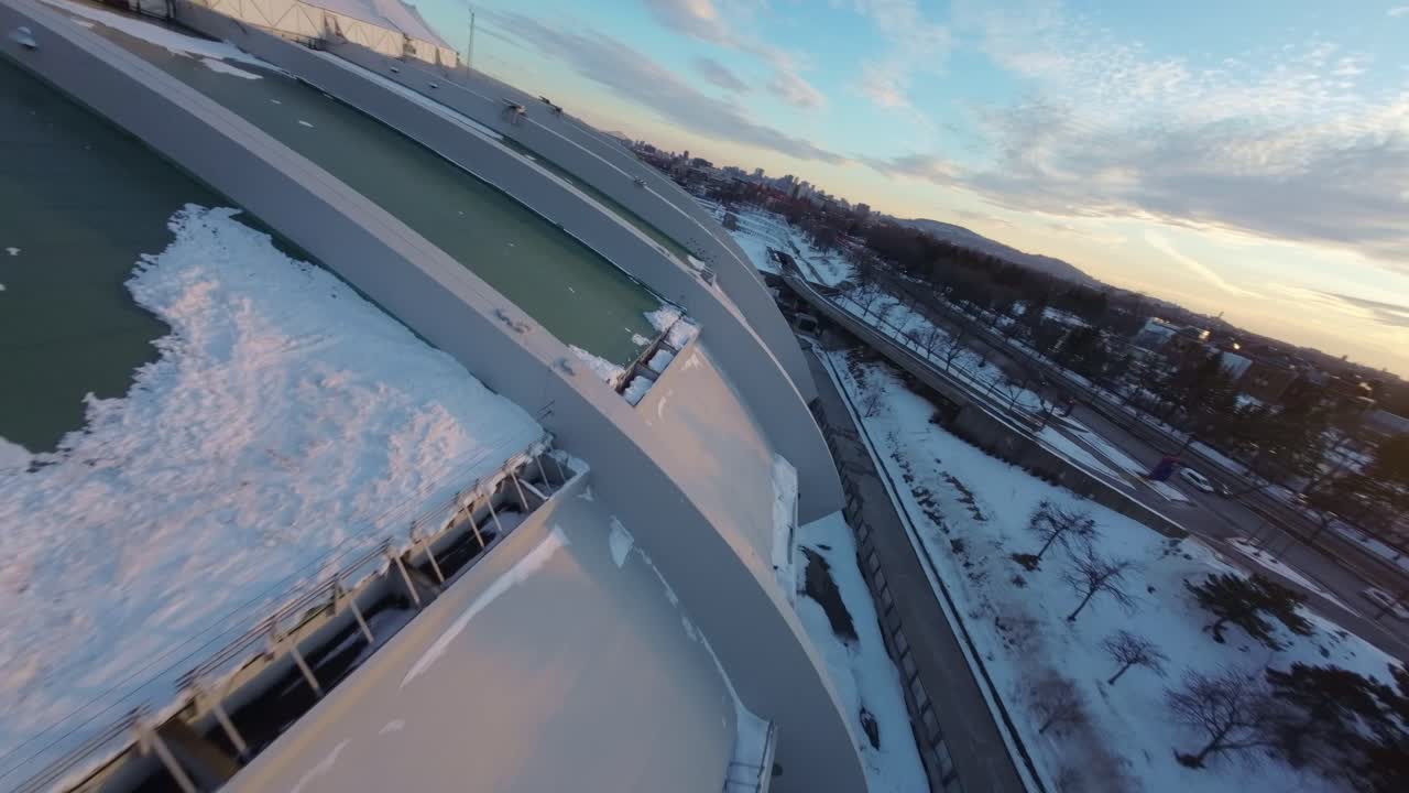 Sunset FPV drone shot of Montreal Olympic Stadium’s snowy roof, capturing cold winter cityscape