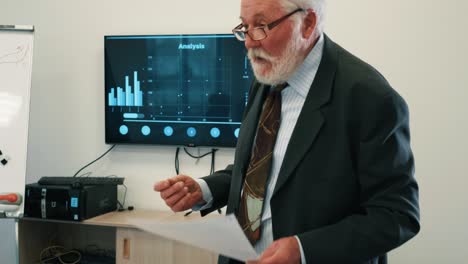 elderly man presenting to her colleagues in conference room business statistics by looking at a tv screen with diagrams and analysis