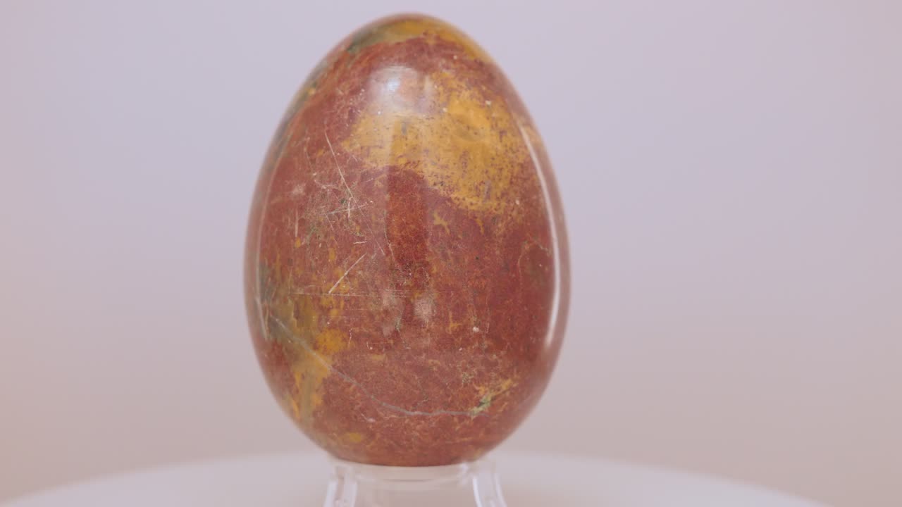 Large yellow and orange Granite egg rotating slowly on a turntable in front of a white background
