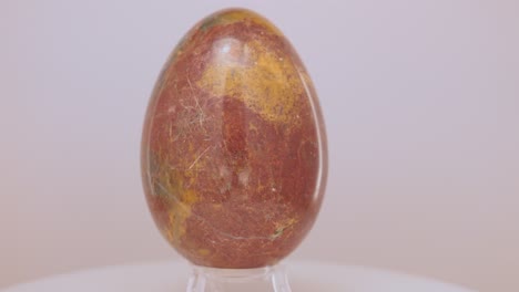 large yellow and orange granite egg rotating slowly on a turntable in front of a white background