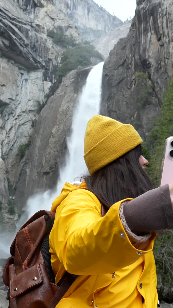 Junge Frau nimmt ein Selfie-Video vor einem majestätischen Wasserfall auf