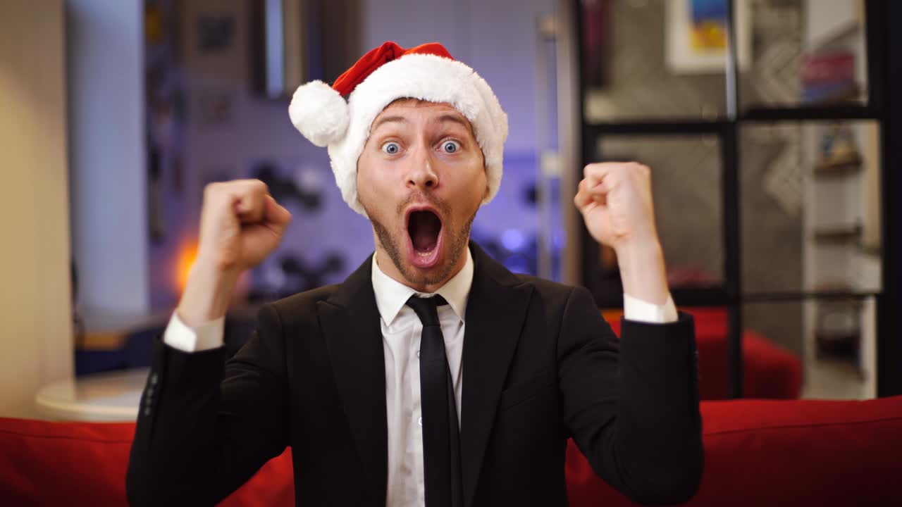 Giovane uomo d'affari con cappello di Babbo Natale rosso, molto felice e gioioso, seduto sul divano. Saldi di Natale, concetto di Boxing Day