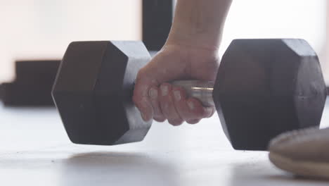 low angle closeup view of determined woman picking up dumbbell from gym floor