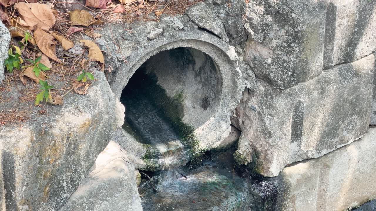 Inquadratura media statica di acque reflue che si scaricano da un canale sotterraneo in cemento in un canale rivestito in pietra.