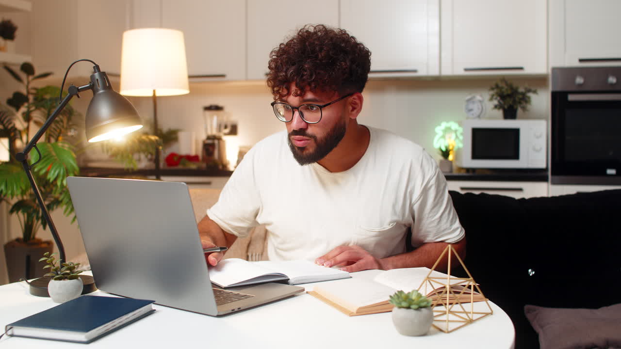 Arabian man studies online on laptop writes notes from video course prepares for exam at night