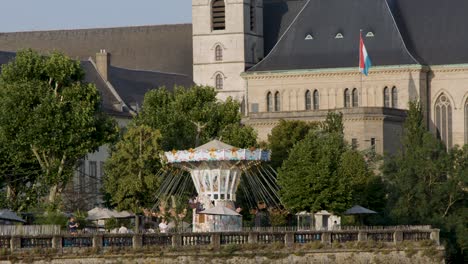 swing carousel rotates outdoors near historic building, daylight, wide shot, steady camera, festive atmosphere
