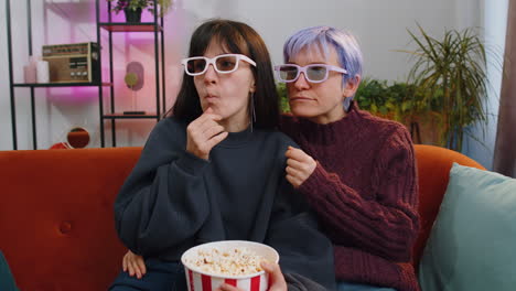 mujeres sentadas en el sofá comiendo palomitas de maíz y viendo interesantes series de televisión, juegos deportivos en línea en casa