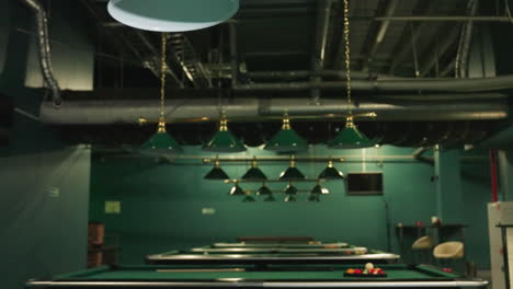 overhead lamps with green shades in billiard room, highlighting golden metallic fixtures and elegant design. pool tables with billiard balls in background add to classic atmosphere