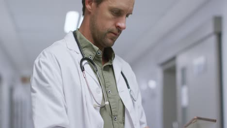 médico caucásico pensativo que usa una tableta digital en el pasillo del hospital