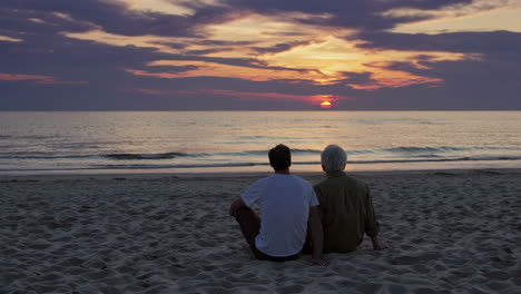 Two men, possibly father and son, embracing on a beach at sunset