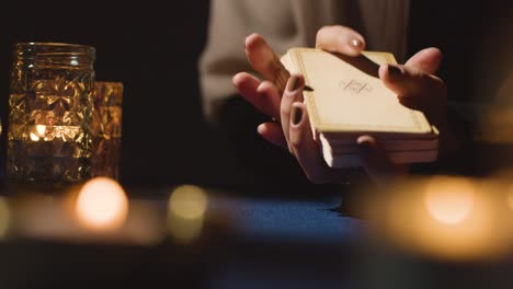 close up of woman shuffling or cutting cards for tarot reading on candlelit table 2