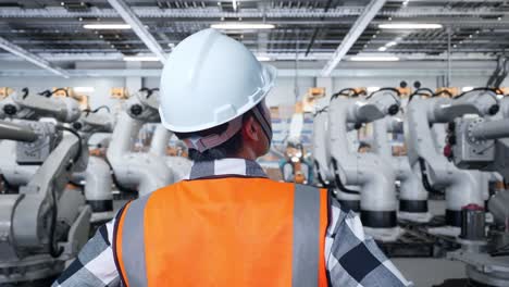 ingeniero observando brazos robóticos en una fábrica