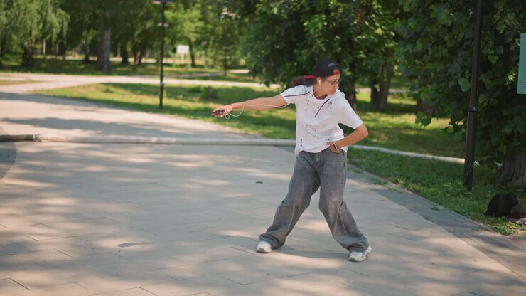 shaded park path streetstyle dancer posing with cap and sunglasses confident male steps through sundappled pavement, directs arms, executes crisp grooves near bench and backpack, contemporary urban