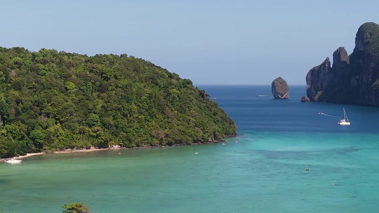 Riprese con drone in panoramica su un resort costiero incastonato tra montagne verdi lussureggianti e acqua turchese.