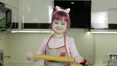 Little-child-girl-in-the-kitchen-dressed-in-apron-and-scarf-with-rolling-pin