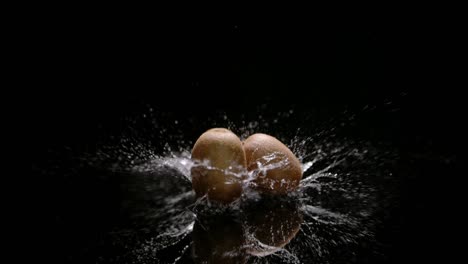 frutos de kiwi que caen sobre la superficie del agua con un gran chapoteo, aislados en negro