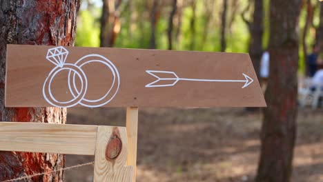 ukraine, yurievka - june 7, 2019. arrow sign into the ground. man hits cake banner post with a stone on event venue. direction info banner for guests installation in pine forest outdoors