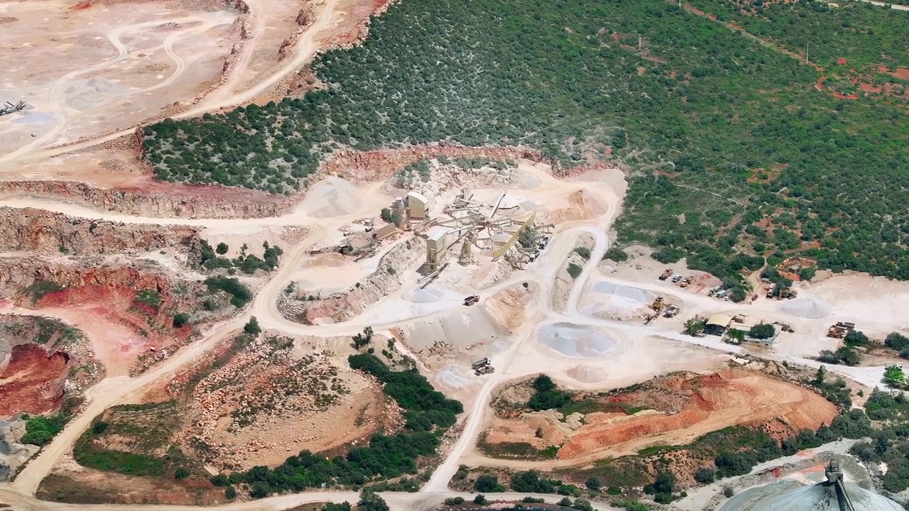 Máquinas pesadas extraem calcário e agregados em uma fábrica de cimento. Esteiras transportadoras levam os materiais para processamento e triagem em um ambiente de mineração a céu aberto.