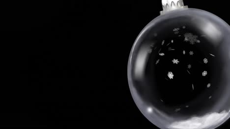 animation of christmas bauble dangling over snow falling on black background