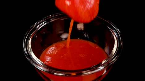 a whole tomato is dropped into a glass bowl filled with tomato sauce, creating a dramatic splash under bright studio lighting with a black background