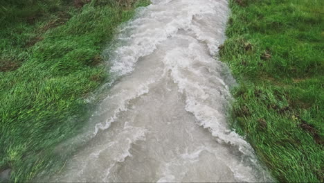 Agua-De-Inundación-Que-Fluye-Ferozmente-A-Través-De-Un-Campo-De-Hierba