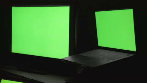 three blank monitors of different sizes on a desktop in a dark room with green screen chroma displayed for compositing purposes