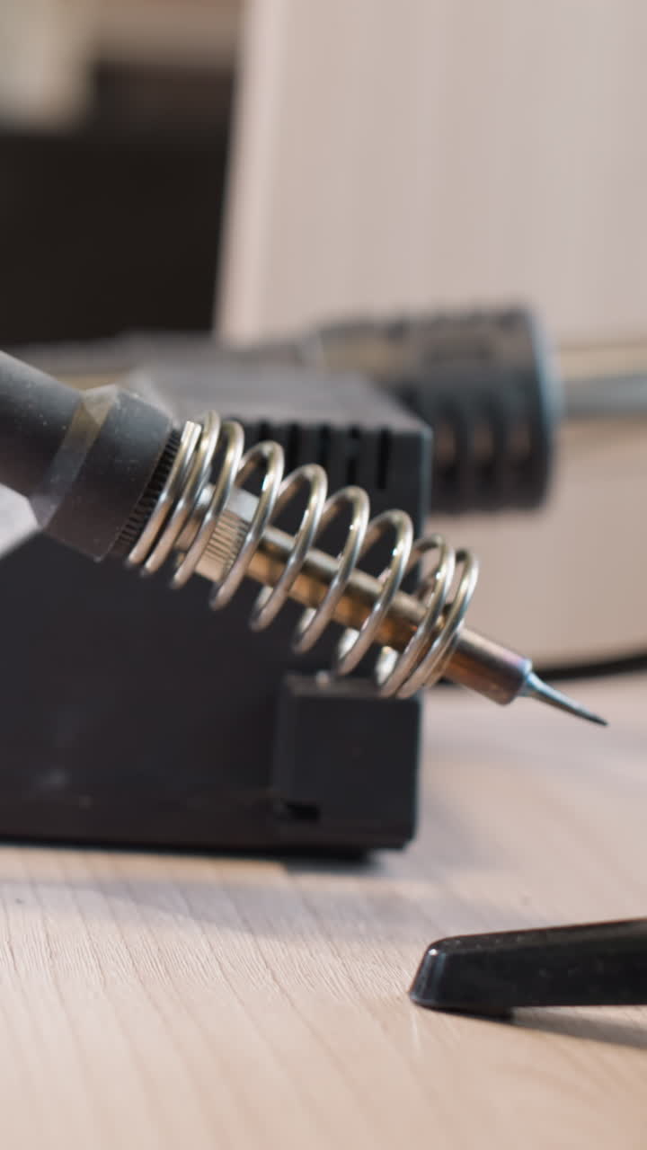 A close-up view of a soldering station with a soldering iron resting in its holder, surrounded by various electronic repair tools on a workbench