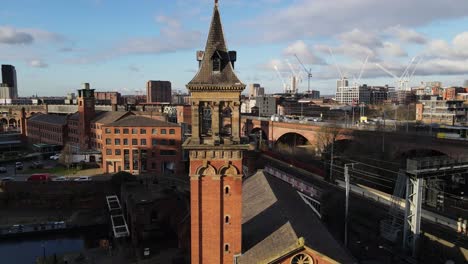 aerial drone flight over deansgate congregational chapel in manchester city centre showing a tram passing by over the viaducts and canal boats in castlefields quays