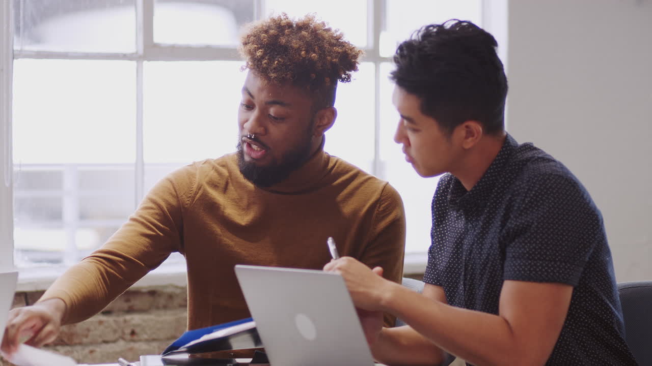 Two male creatives discussing paperwork with an unseen colleague in a meeting room, close up