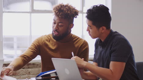 two male creatives discussing paperwork with an unseen colleague in a meeting room, close up