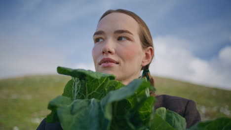 girl showing organic vegetable closeup. woman with braids standing green field