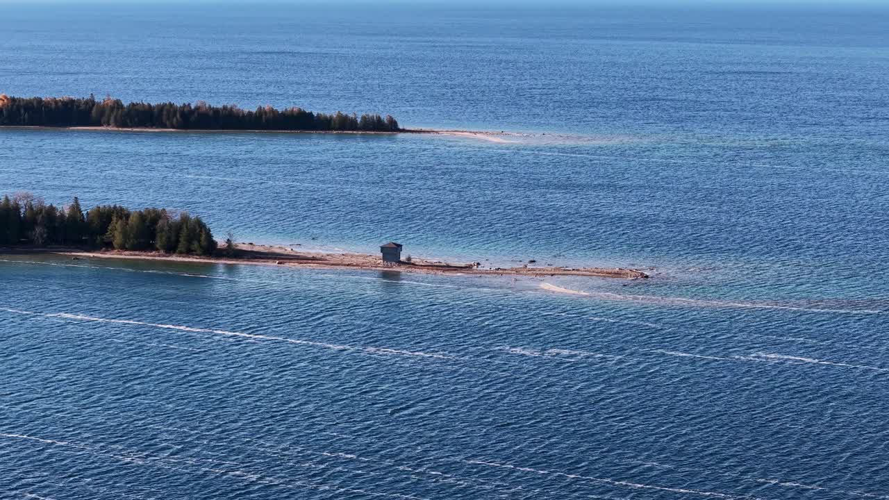 Aerial drone shot of tranquil blue lake with thin sandy islands and evergreen forest coastline