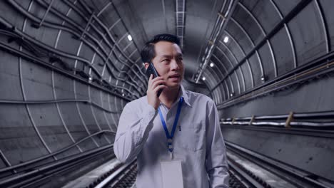 asian male professional worker standing in underground subway tunnel, he pick the phone up and started to speaking with it