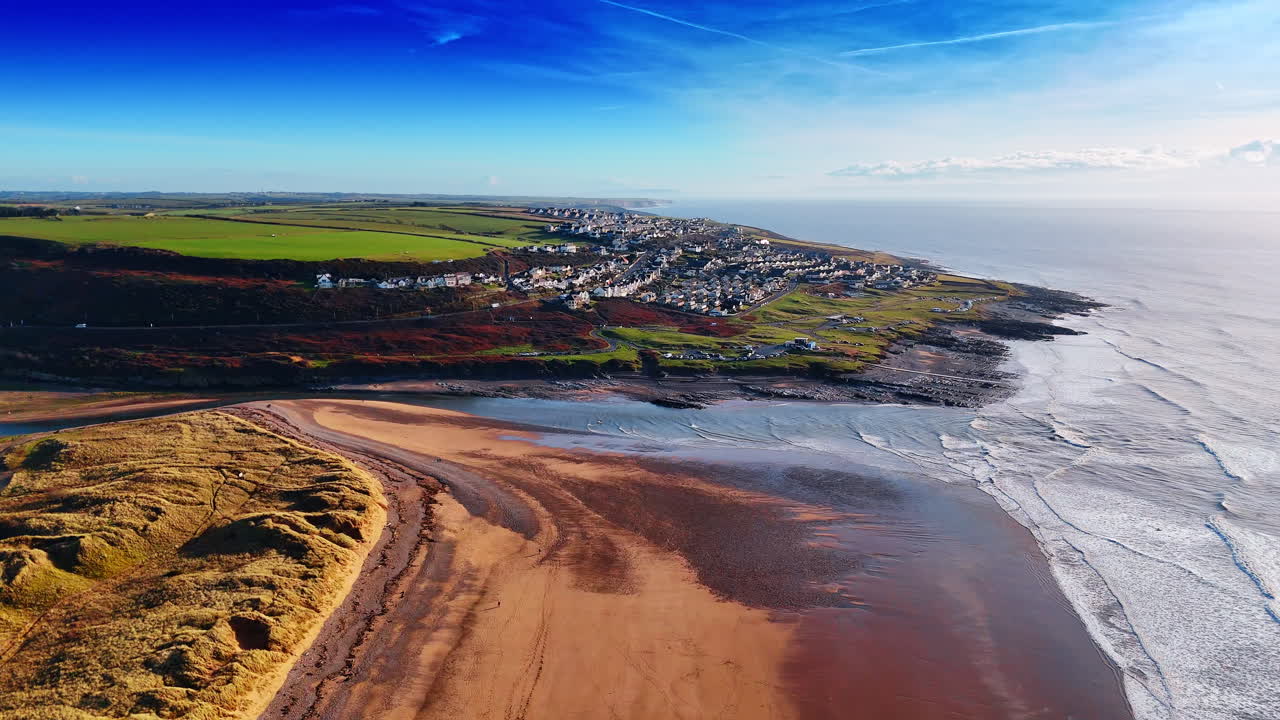 Panoramablick auf eine Küstensiedlung und Sandbucht. Aufnahme aus großer Höhe von Häusern auf einem Hügel mit Blick auf einen breiten Sandstrand und Meereswellen.
