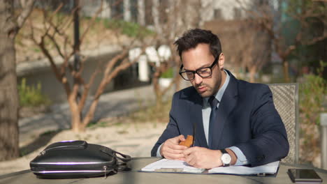 young business man 30s wear blue suit work with paper documents sit in chair rest relax in spring city park sunshine outdoors in nature