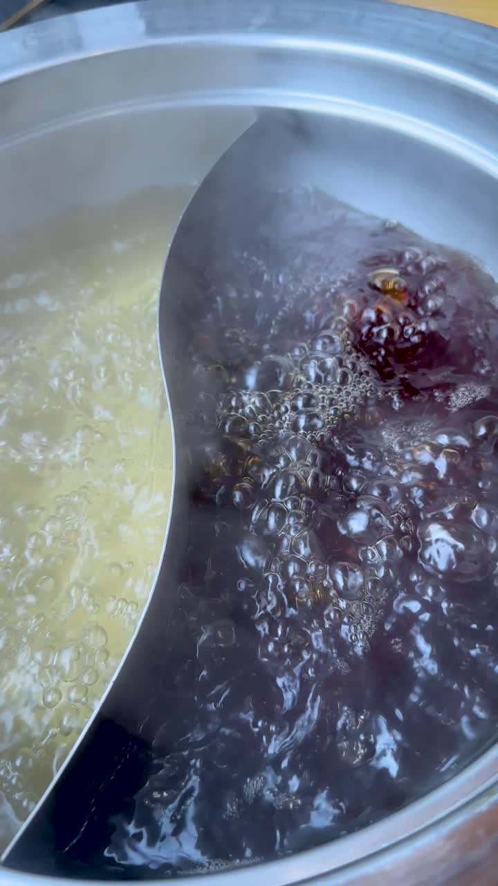 Close-up of steaming dual broth hotpot boiling vigorously, overhead view, bright indoor lighting
