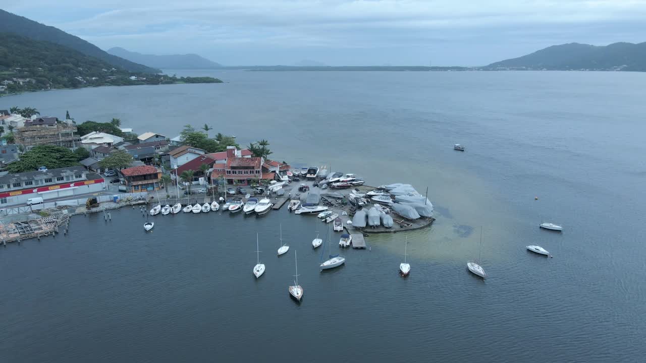 Aerial View of a Coastal Marina with Boats and Mountains Under Overcast Sky