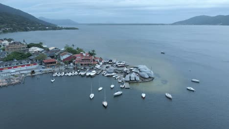 aerial view of a coastal marina with boats and mountains under overcast sky