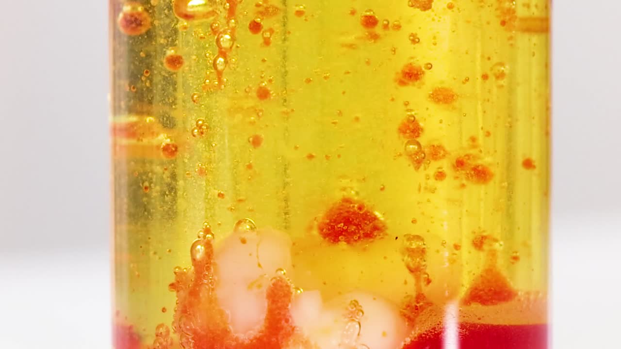 Red blobs dynamically interact within a yellow liquid, creating a mesmerizing visual effect.