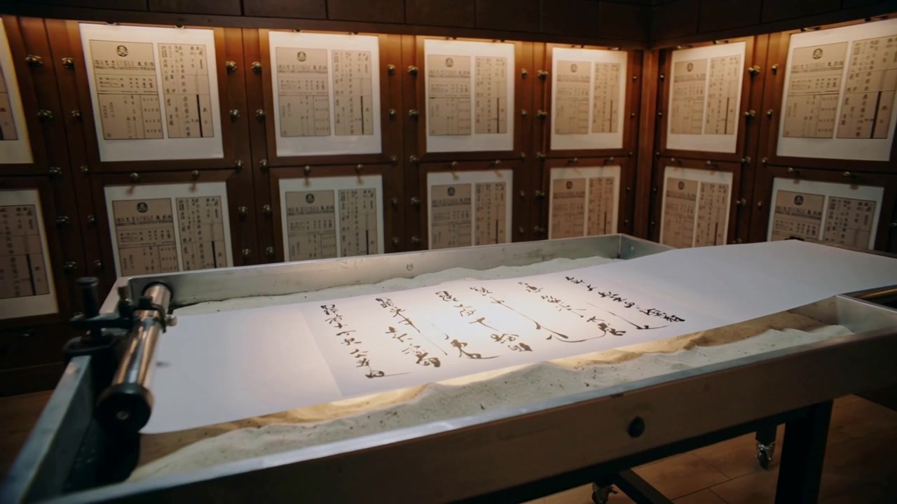Panning camera revealing ink scroll on padded table in archive room for study, roller clamp visible