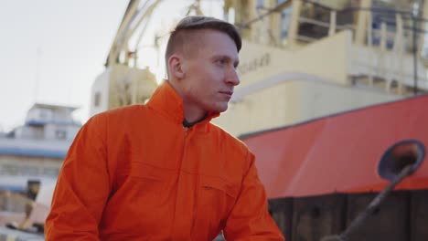 Harbor-master-in-orange-uniform-sitting-in-front-of-a-large-ship-in-harbour-and-smiling