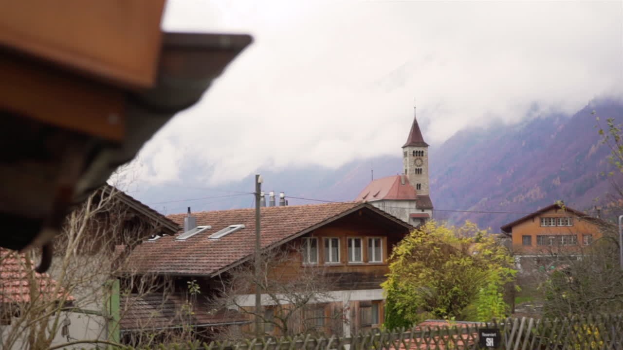 Inquadratura rivelatrice con panoramica da sinistra a destra, con la Chiesa Evangelica Riformata di Brienz sullo sfondo, in una giornata nebbiosa.
