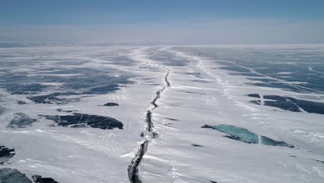 aerial tilt shot of the huge deep crack on snow covered frozen ice surface of lake baikal. natural landmark. winter landscape. popular touristic destination.