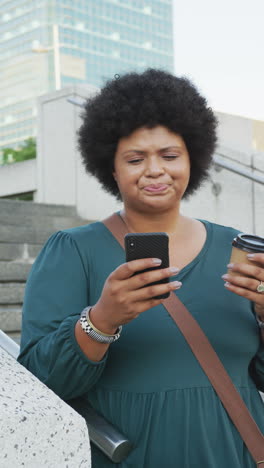 vertical video of plus size biracial woman walking on street with coffee and smartphone